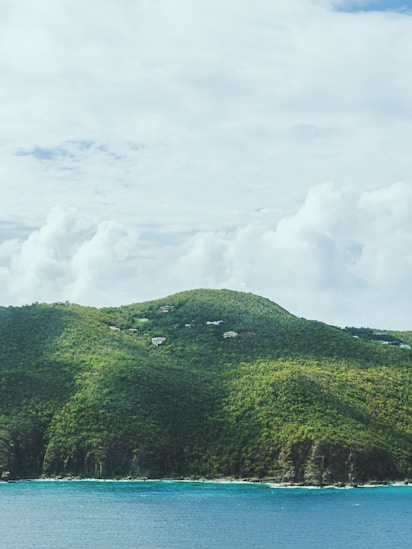 Colline verdoyante et luxuriante surplombant une mer turquoise sous un ciel nuageux